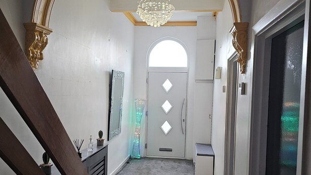 Un pasillo con un arco imponente, un candelabro, una puerta con ventanas de forma de diamante y una escalera.