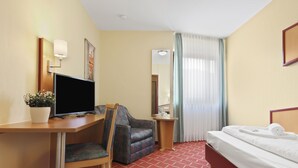 A hotel room with a desk, chair, TV, bed, and a small table with a mirror. - XZLLENZ light, parking, 24h digital check in and access, pet friendly (Oberasbach)