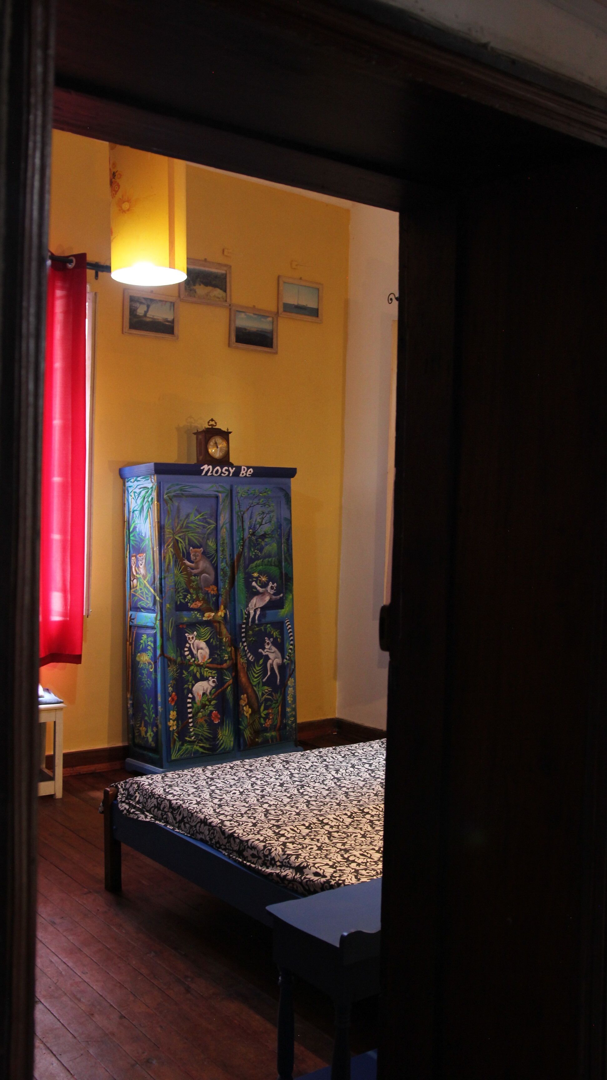 A room with a bed, a cabinet with artwork, a red curtain, and a wall clock.