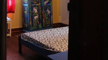 A room with a bed, a cabinet with artwork, a red curtain, and a wall clock.