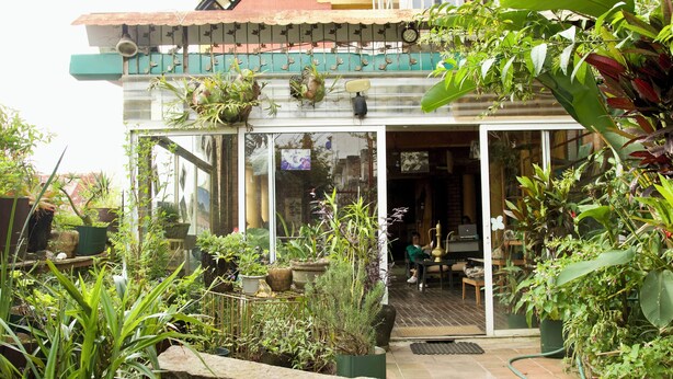 A house with a glass door leading to a patio area with potted plants and a stone bench. - Le Karthala (Antananarivo)