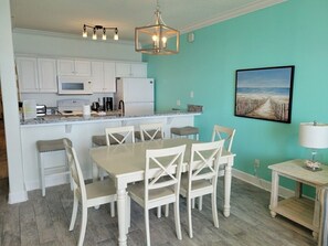 A kitchen with white cabinets, a dining table with chairs, a hanging light fixture, and a framed picture on the wall. - Beach side with a great view - 3-bedroom condo on Panama City Beach (Panama City Beach)