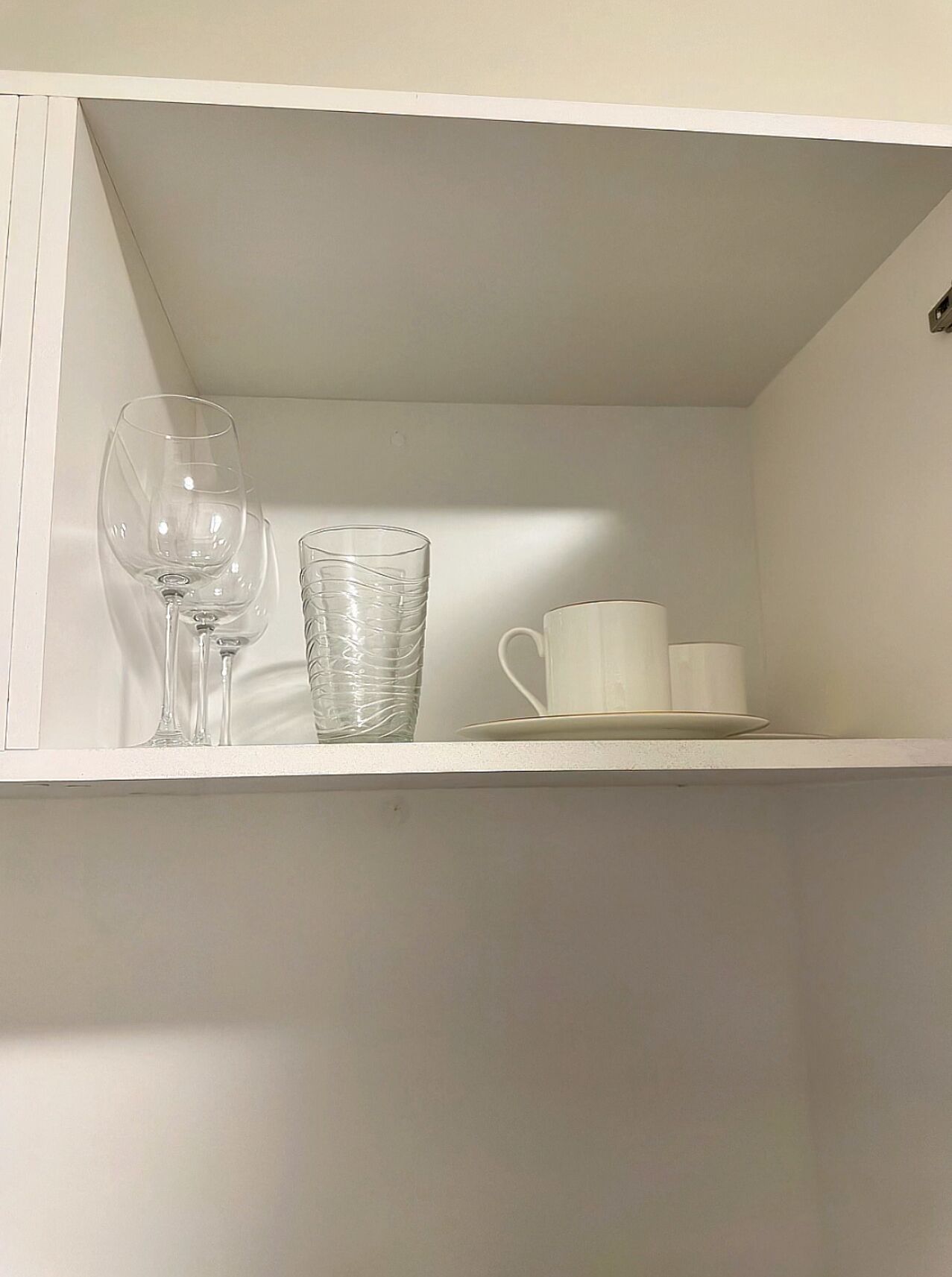 Ein weißes Regal mit einem Weinglas, einem Glas und zwei weißen Tassen.