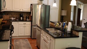 A kitchen with white cabinets, a stainless steel refrigerator, a black countertop, and a hanging light fixture.