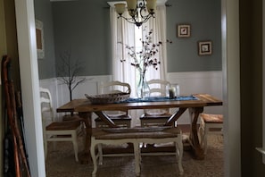 Et spiseområde med et træbord, hvide stole, en vase med blomster og en lysekrone.