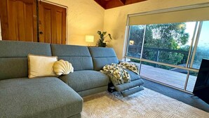 A living room with a sectional sofa, a ceiling fan, and a large window with a view. - Treetop Ocean Views at Maslin Beach Coastal Escape (Maslin Beach)