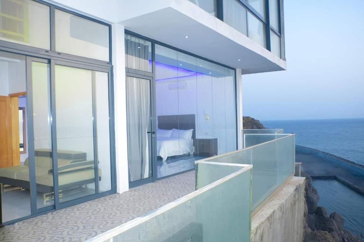 A modern hotel room with a glass balcony overlooking the sea.