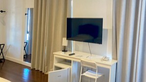 A hotel room with a white desk, a flat-screen TV, a chair, a bed, and a window with curtains. - The View Hotel CV (Sao Filipe)