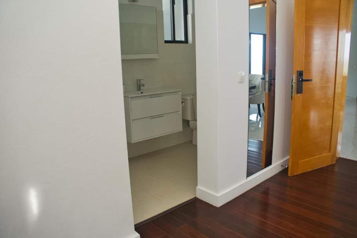 A hallway leading to a bathroom with a wooden door and a mirror above the sink.
