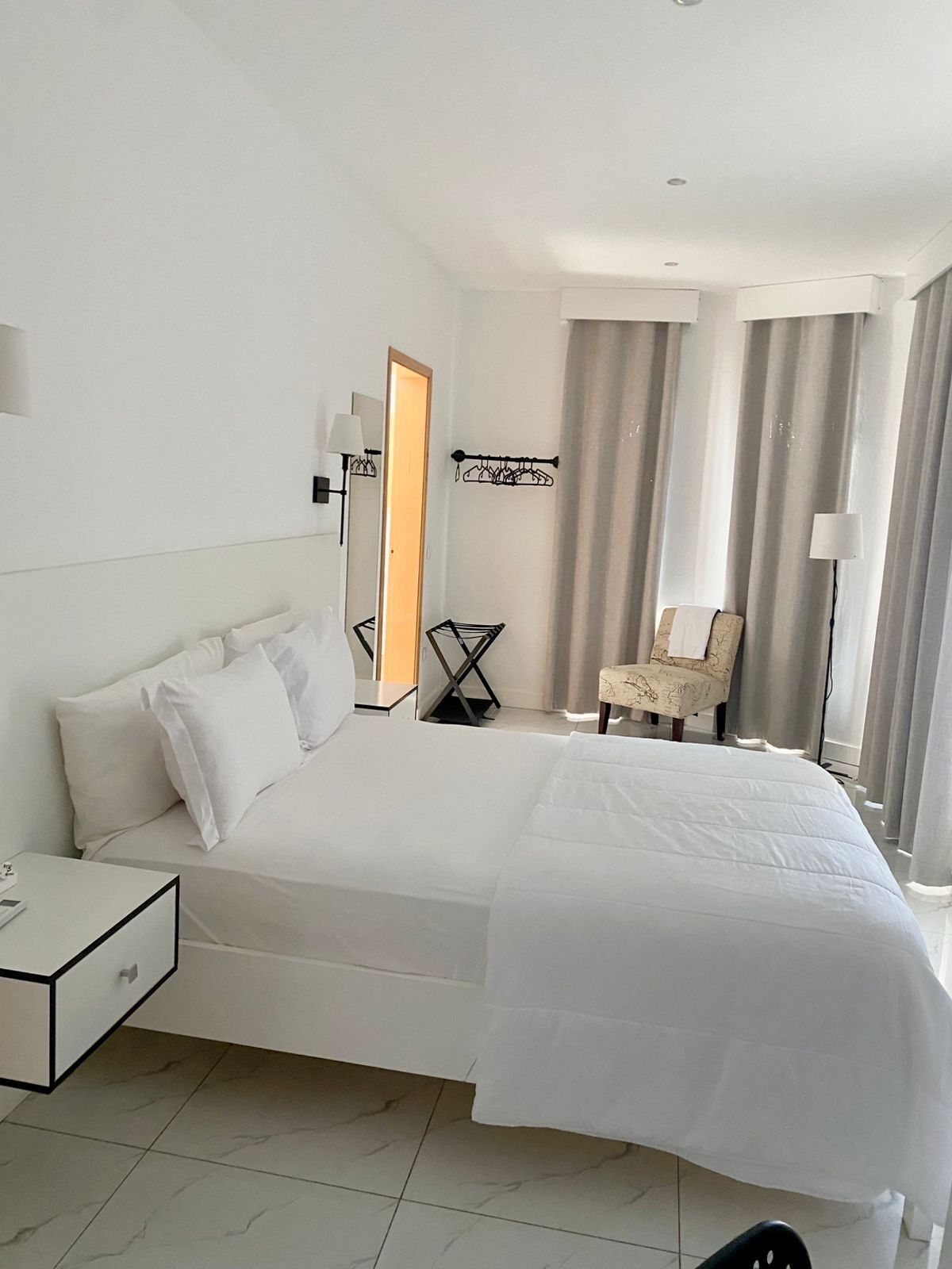 Una habitación de hotel con una cama grande, una silla, un perchero y un espejo.
