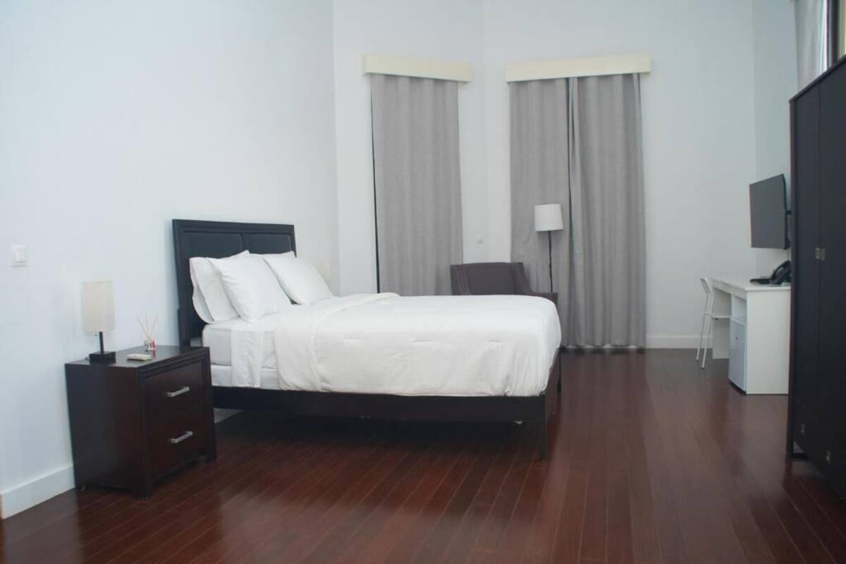 A hotel room with a bed, a desk, a chair, a TV, and curtains.