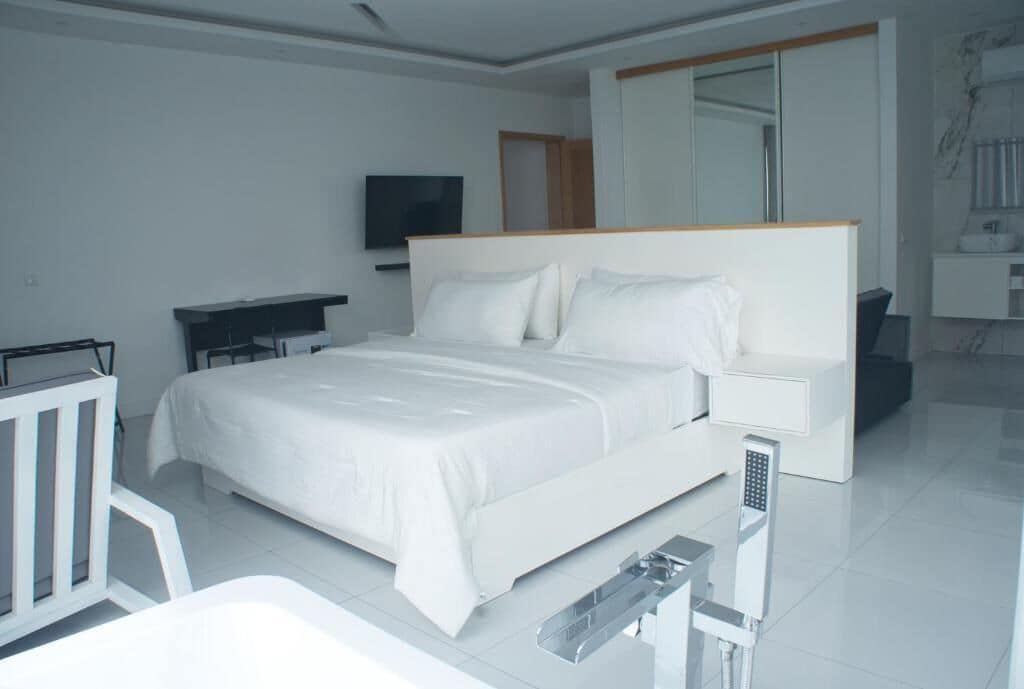 A modern hotel room with a large bed, a desk, a television, and a bathroom with a mirror and sink.