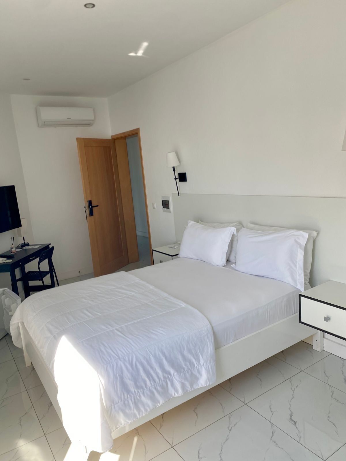 Une chambre à coucher comprenant un lit, un bureau, une chaise, une table de chevet et une lampe fixée au mur.