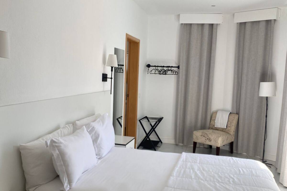 A hotel room with a bed, a chair, a desk, and a mirror.