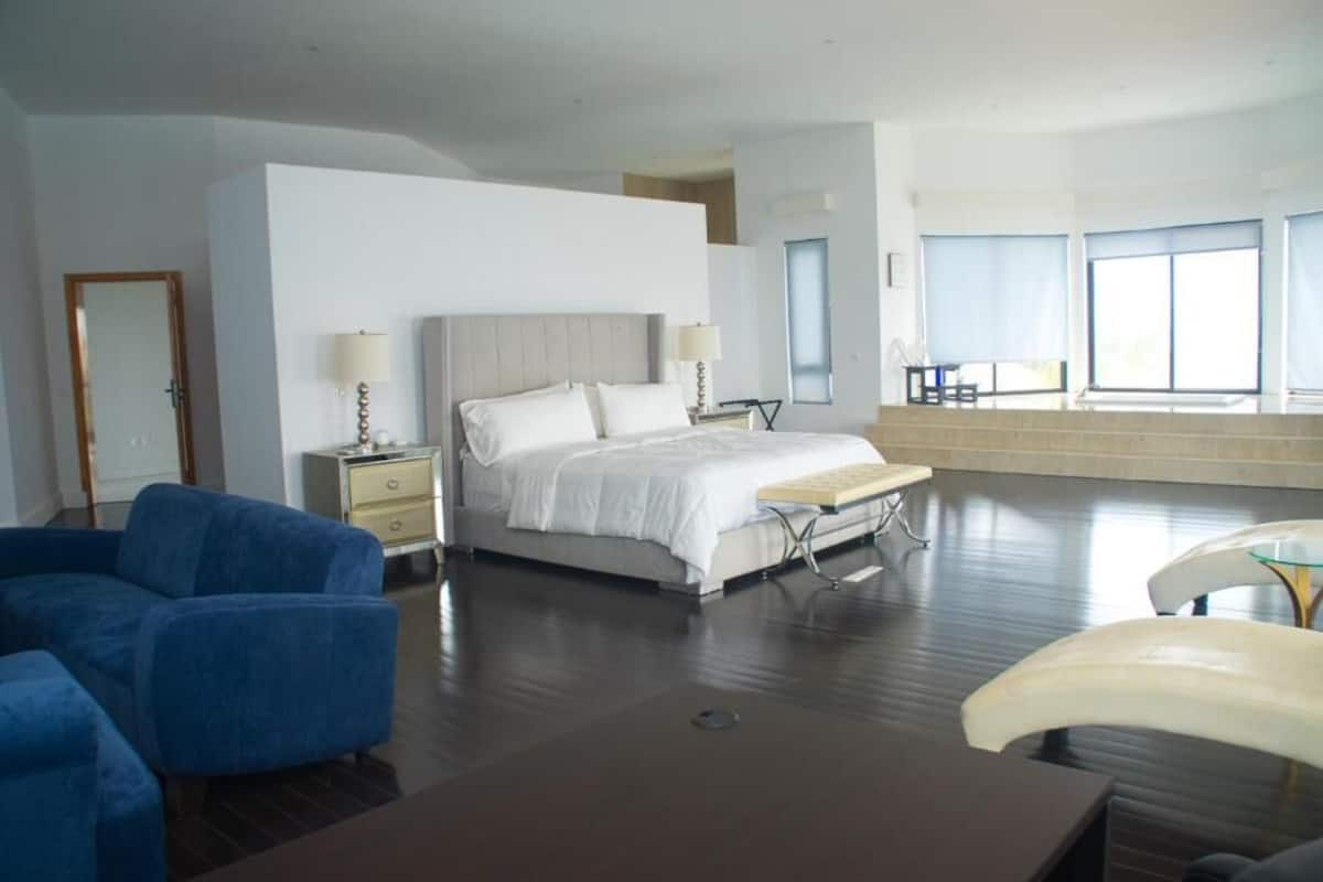 A modern hotel room with a large bed, a desk, a chair, and a sofa.