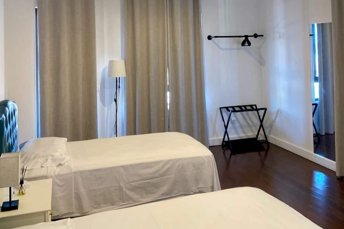 A hotel room with two beds, a desk, a lamp, and a chair.