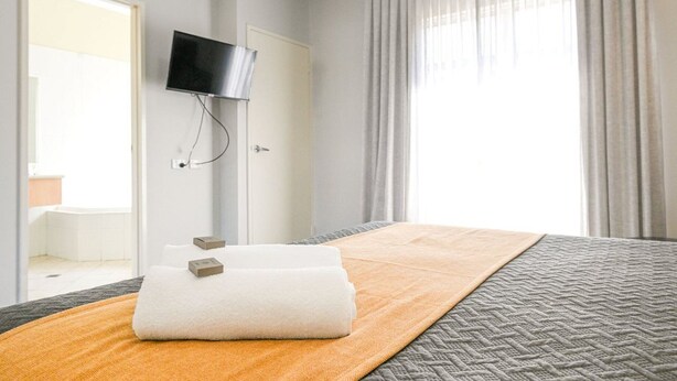 A hotel room with a bed, a TV mounted on the wall, and a window with curtains. - Collie Ridge Motel (Collie)