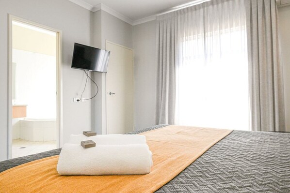 Een hotelkamer met een bed, een aan de muur bevestigde televisie en een raam met gordijnen.