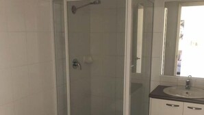 A bathroom with a glass-enclosed shower, a toilet, and a sink with a mirror. - Collie Ridge Motel (Collie)