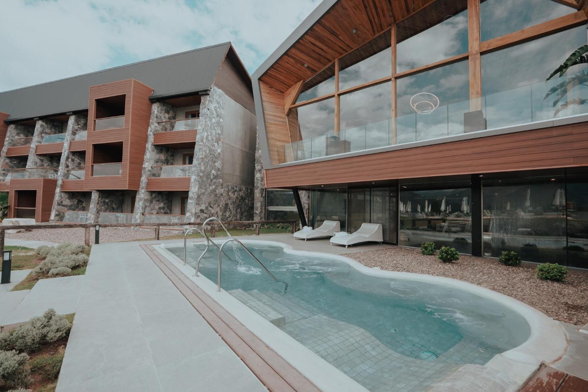 Un bâtiment moderne doté d’une piscine, de chaises longues et d’une façade en pierre.