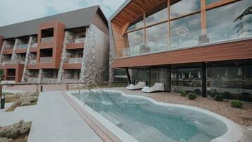 Un bâtiment moderne doté d’une piscine, de chaises longues et d’une façade en pierre.