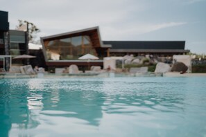 Ein Swimmingpool mit Liegestühlen und Sonnenschirmen, moderne Gebäude im Hintergrund.