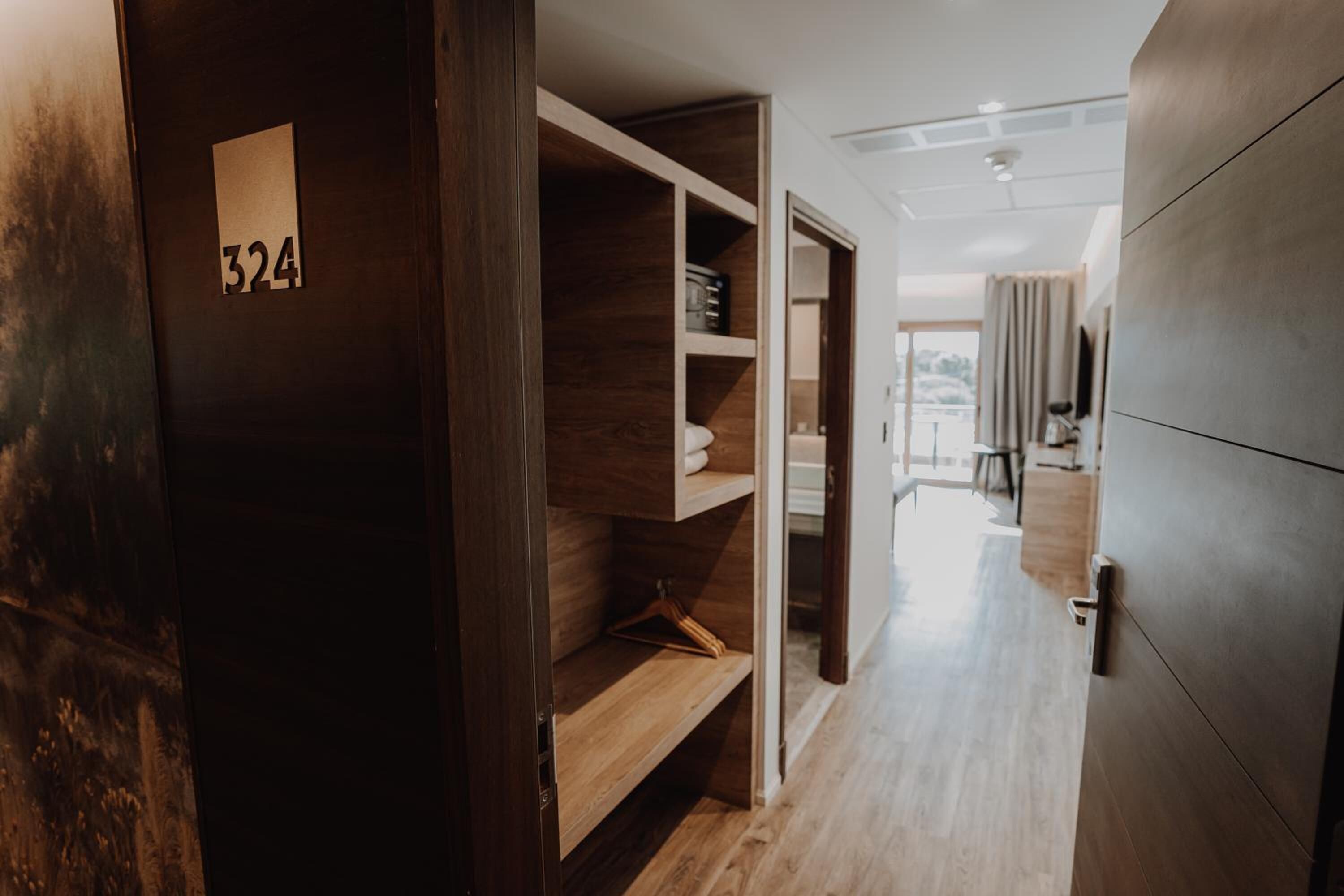 A modern hotel room with a wooden wardrobe, a number 324 sign, and a view of the city through the window.