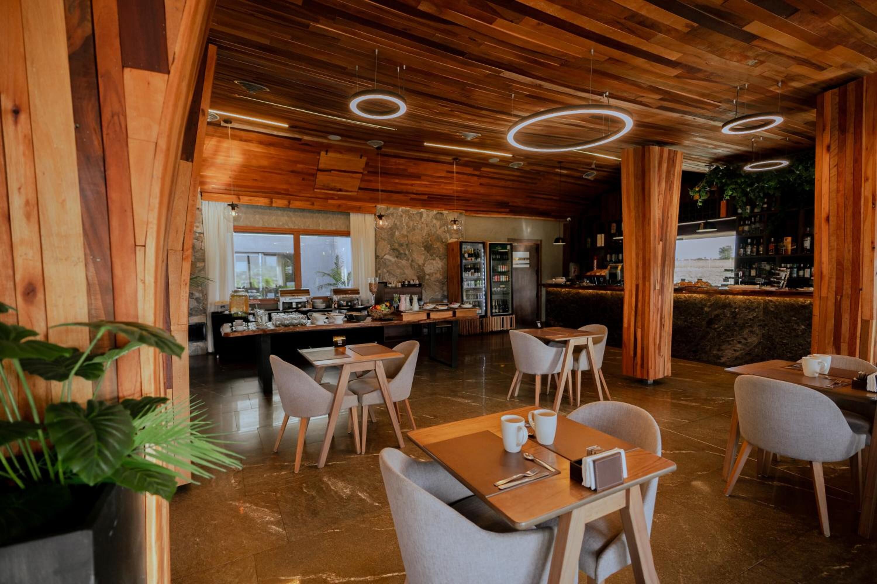 A modern restaurant with wooden ceiling, circular lighting, and a bar area.