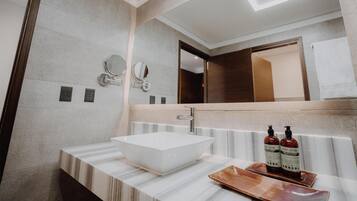 Ein modernes Badezimmer mit einem großen, rechteckigen Waschbecken, zwei wandmontierten Spiegeln und einem rechteckigen Spiegel über dem Waschbecken. Auf der Ablagefläche stehen zwei Flaschen Körperlotion.