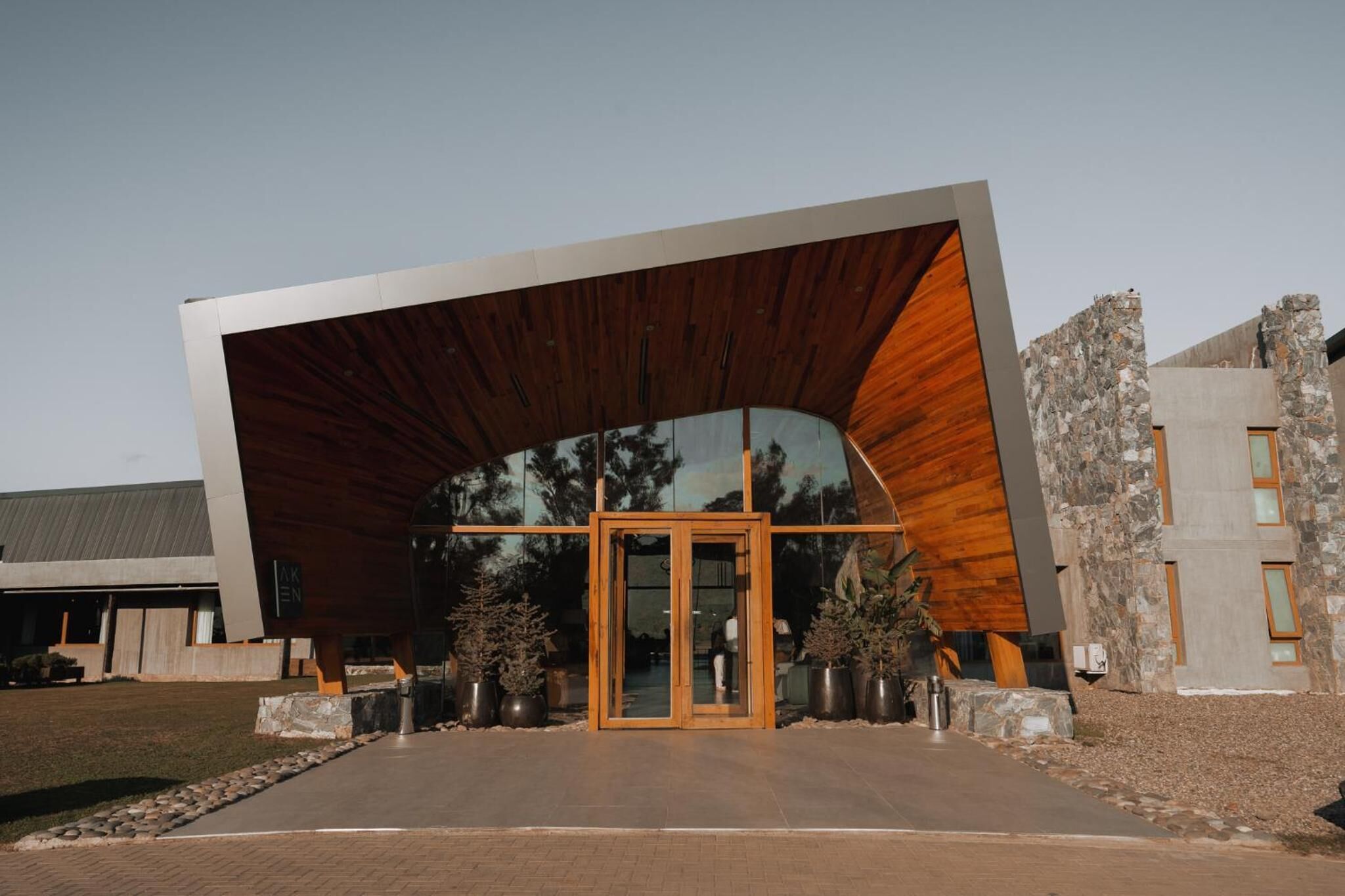 Un bâtiment moderne doté d’un toit en bois incurvé, d’une entrée en verre et de murs en pierre.
