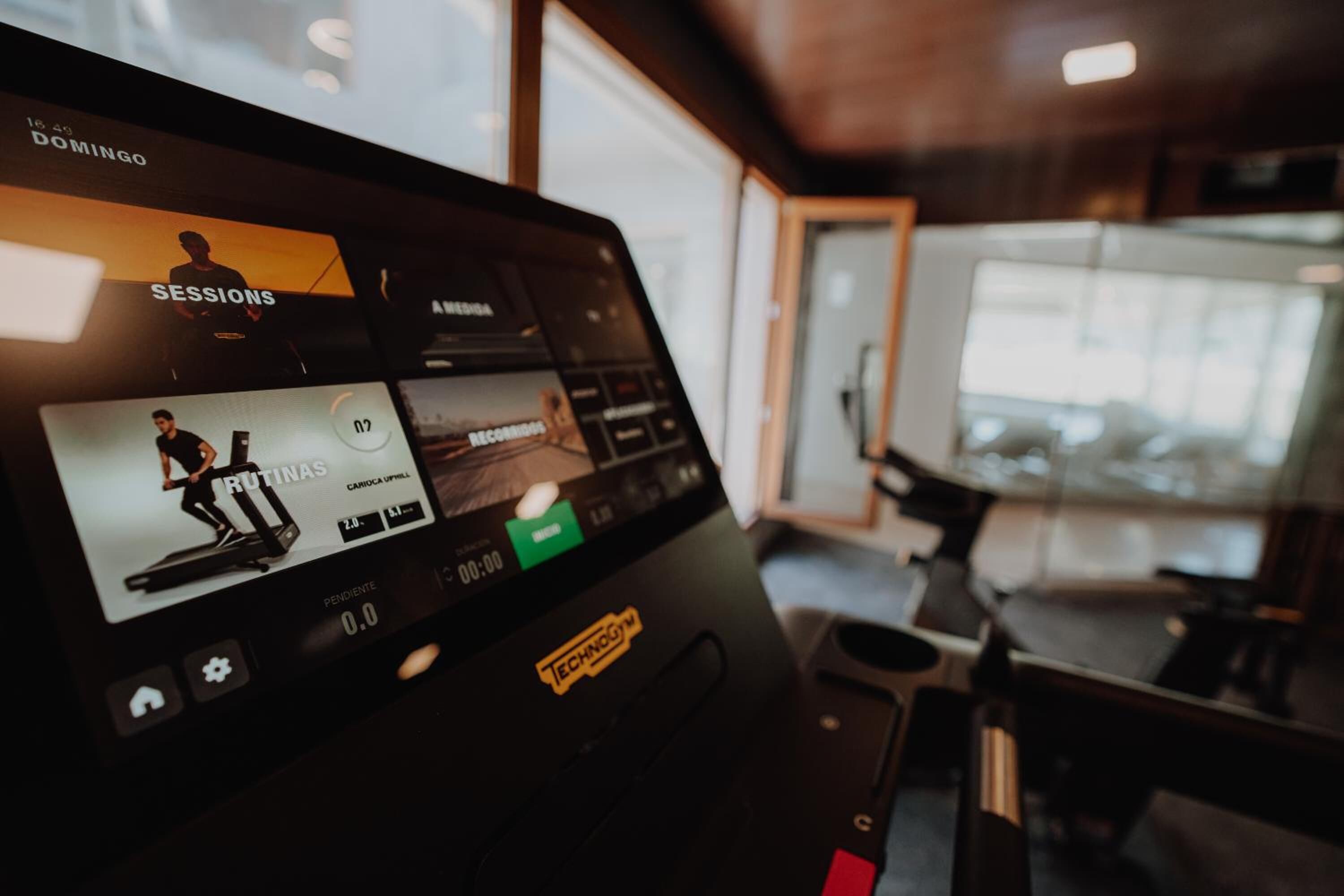 A digital screen with workout routines and a treadmill in a modern gym setting.