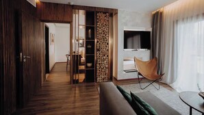 Een moderne woonkamer met houten vloer, een bank, een fauteuil, een televisie en een eethoek met een tafel en stoelen.