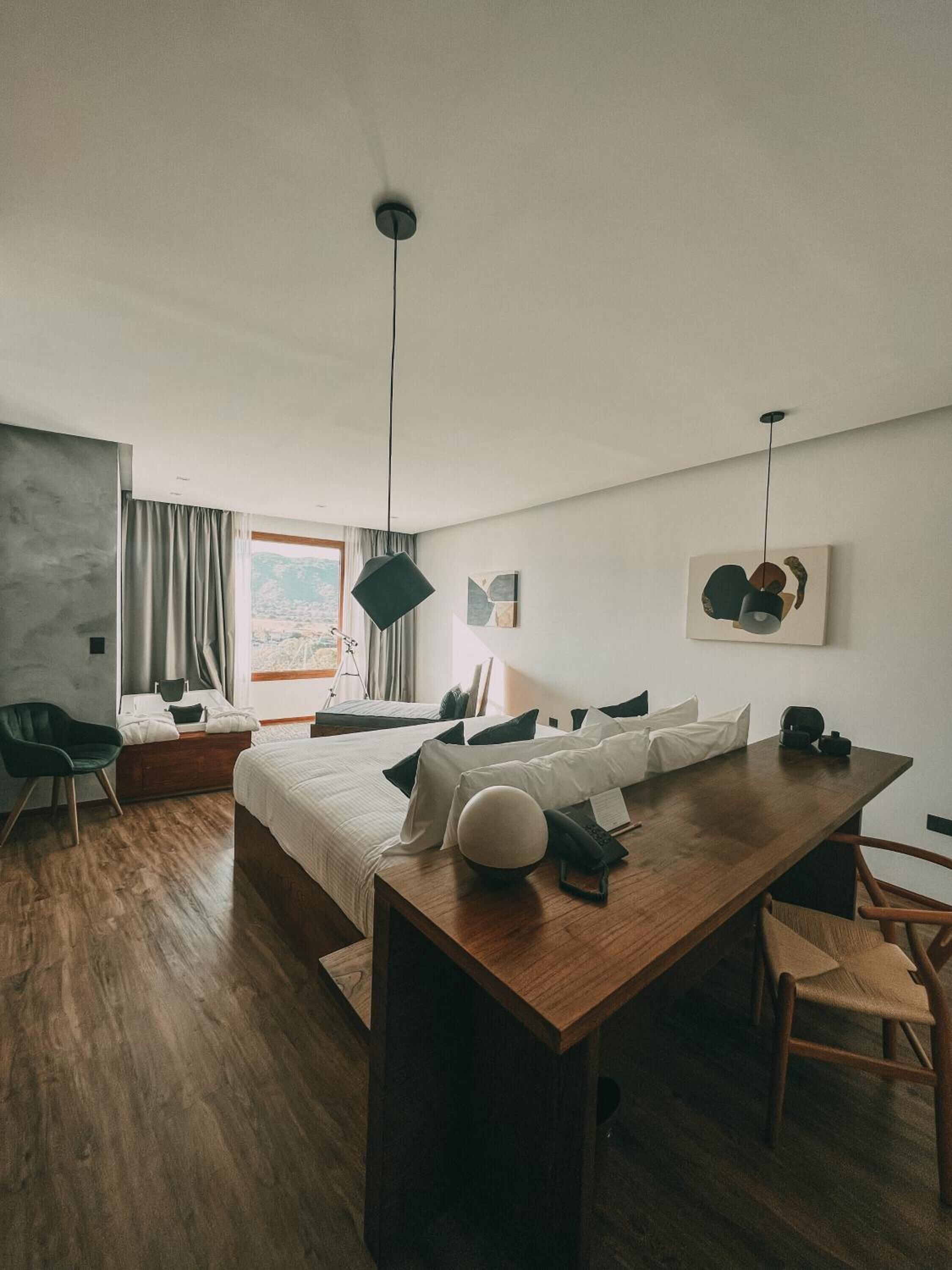 Una habitación de hotel moderna con una cama grande, un escritorio de madera, una silla, una lámpara de escritorio y obras de arte en las paredes.
