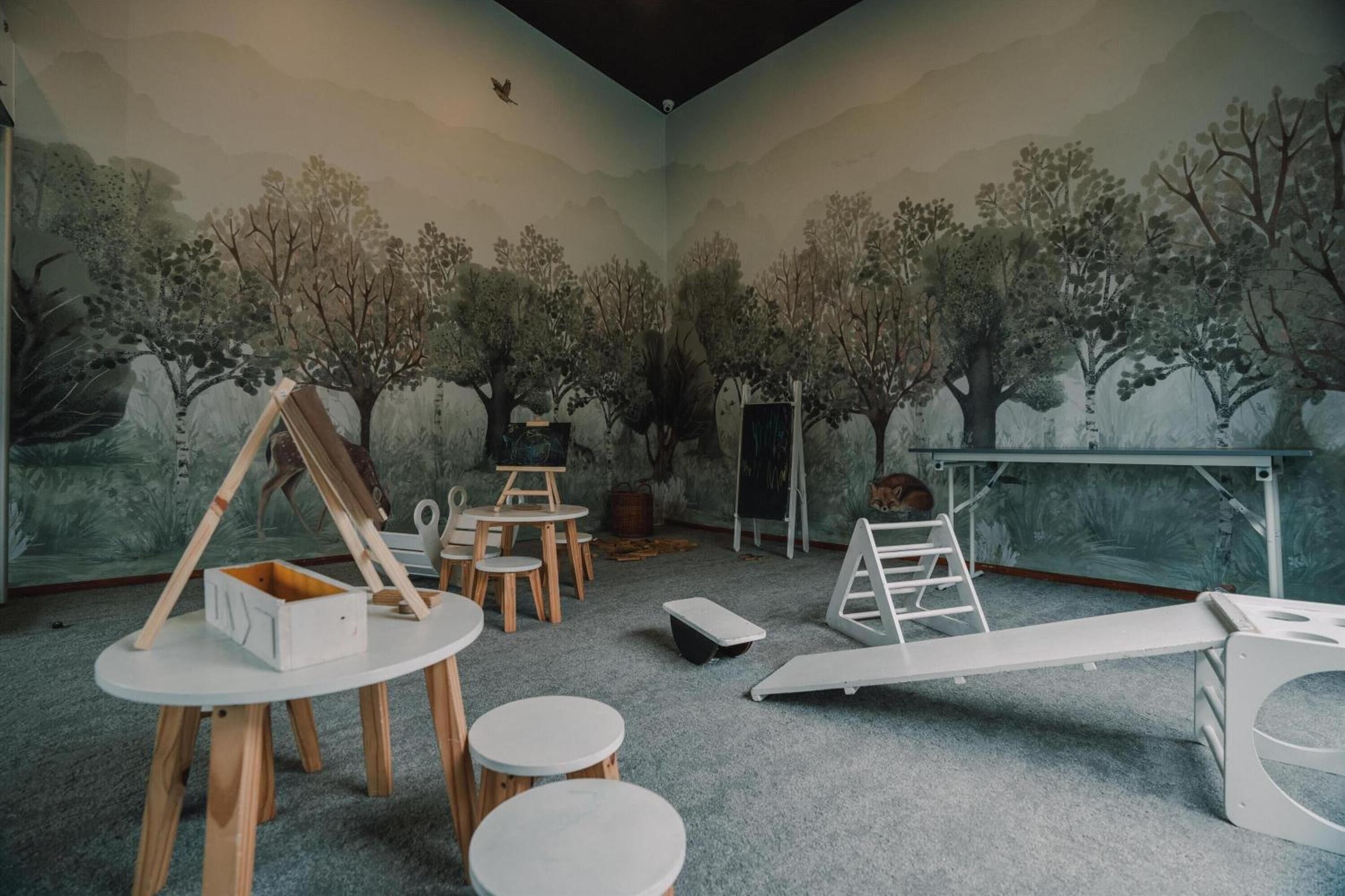 A room with a mural of trees, a whiteboard, and a whiteboard stand.