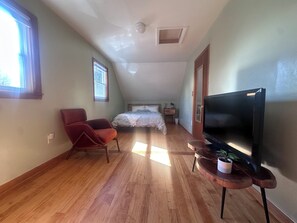 A room with a bed, a red chair, a TV, and a small table with a plant. - Family-Friendly 3BR Home Burke Mountain & Kingdom Trails Quiet, Sunlit, Sleeps 6 (Lyndon)