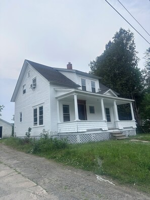 A two-story white house with a porch, a chimney, and a large tree in the background.