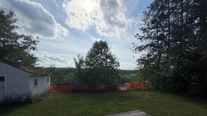 Ett trädäck, en vit byggnad och ett inhägnat område med träd i bakgrunden.