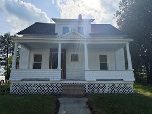 A two-story white house with a front porch, a central entrance, and a small front yard.