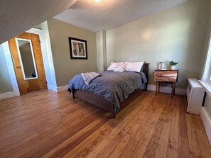 A bedroom with a bed, a nightstand, a mirror, and a radiator.