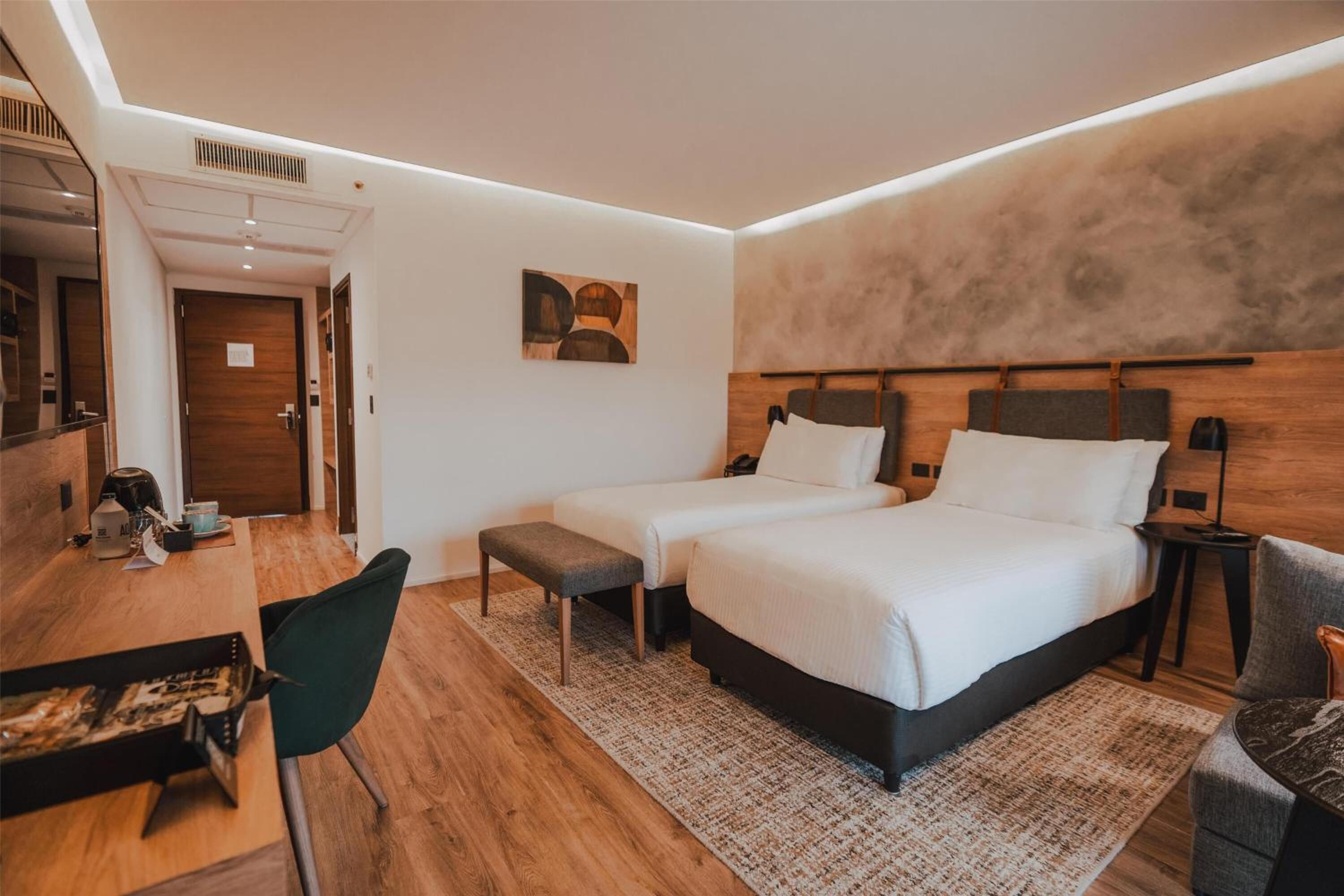 Una habitación de hotel moderna con piso de madera, dos camas, un escritorio con silla y una mesita.