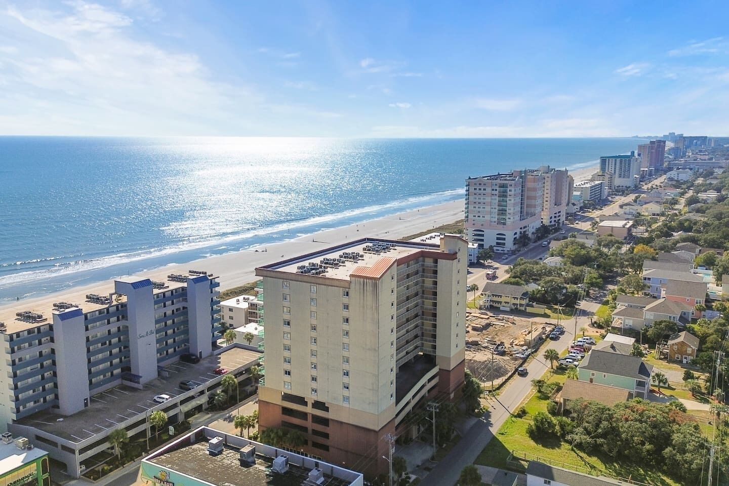 Ein Hotel an der Küste mit mehreren Etagen, einem Parkplatz und Blick auf den Strand.