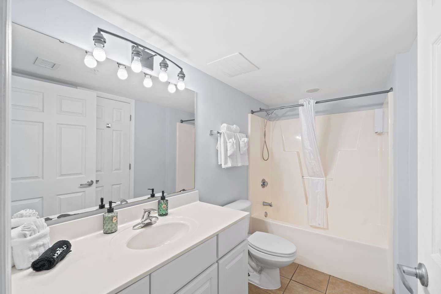 Un baño con lavamanos doble, inodoro, ducha con cortina y espejo con iluminación.