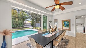 Uma área de refeições com vista para a piscina, um ventilador de teto e uma cozinha ao fundo.