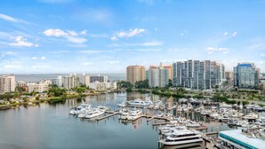 Uma marina com vários barcos atracados, cercada por edifícios altos e uma superfície de água calma.