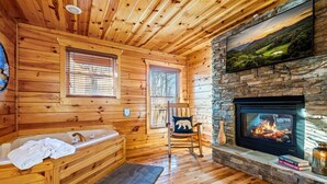 L’intérieur d’une cabane en rondins, avec une cheminée en pierre, des murs en bois, une baignoire et une grande fenêtre.