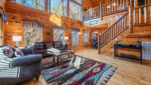 Une cabane en bois spacieuse, dotée d’un grand salon, d’un escalier et offrant une vue sur la forêt environnante.