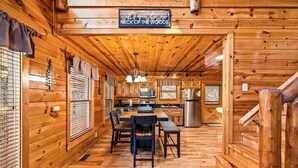 L’intérieur d’un chalet en bois comprend un coin repas, une cuisine et une enseigne sur laquelle on peut lire : « NECK OF THE WOODS ».
