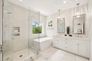 A modern bathroom with a glass-enclosed shower, a freestanding bathtub, and a vanity with a large mirror.