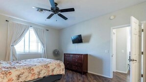 Un dormitorio con cama, ventilador de techo, televisor, cómoda y una puerta.