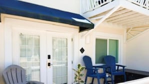 A balcony with a white railing, a grey Adirondack chair, and two blue chairs.